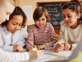 Kinder sitzen an Tisch und schreiben