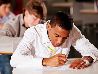 Schüler schreibt über Tisch gebeugt